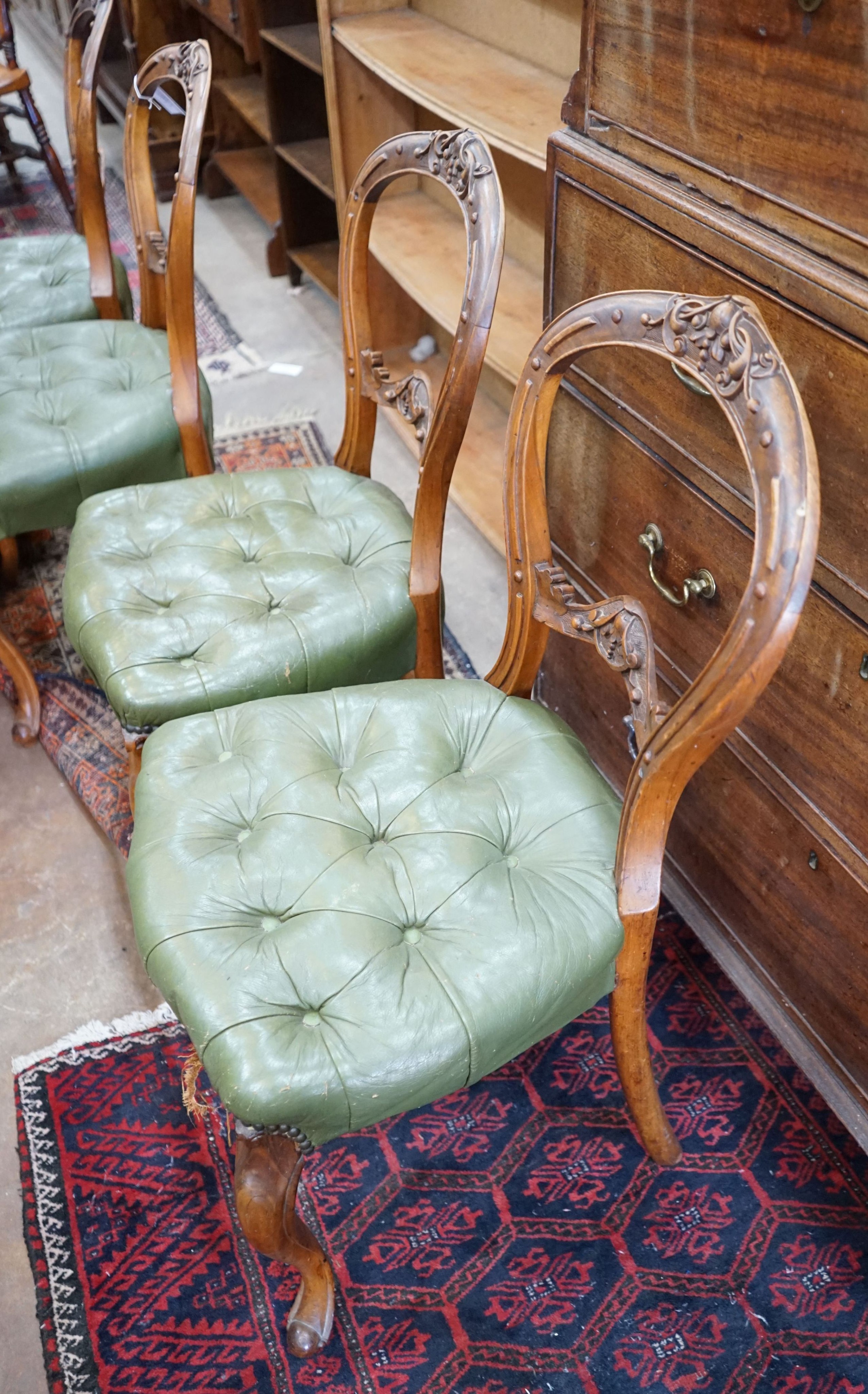 A set of six Victorian carved walnut and buttoned green leather spoon back dining chairs